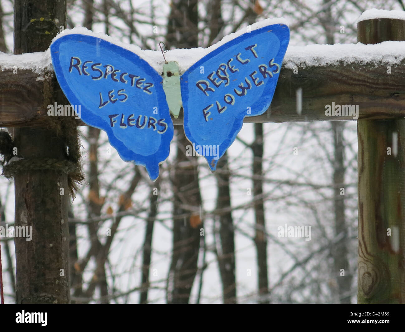 Snow covered butterfly shaped sign in French 'respectez les fleurs' and in English 'respect flowers'. Stock Photo