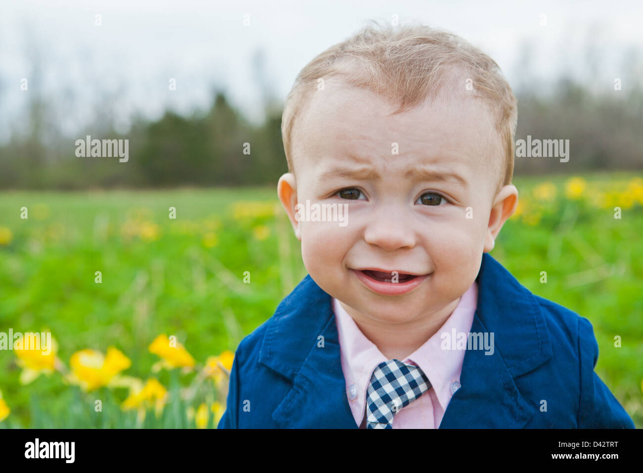 A little boy in a pink shirt, blue jacket and tie, standing and smiling