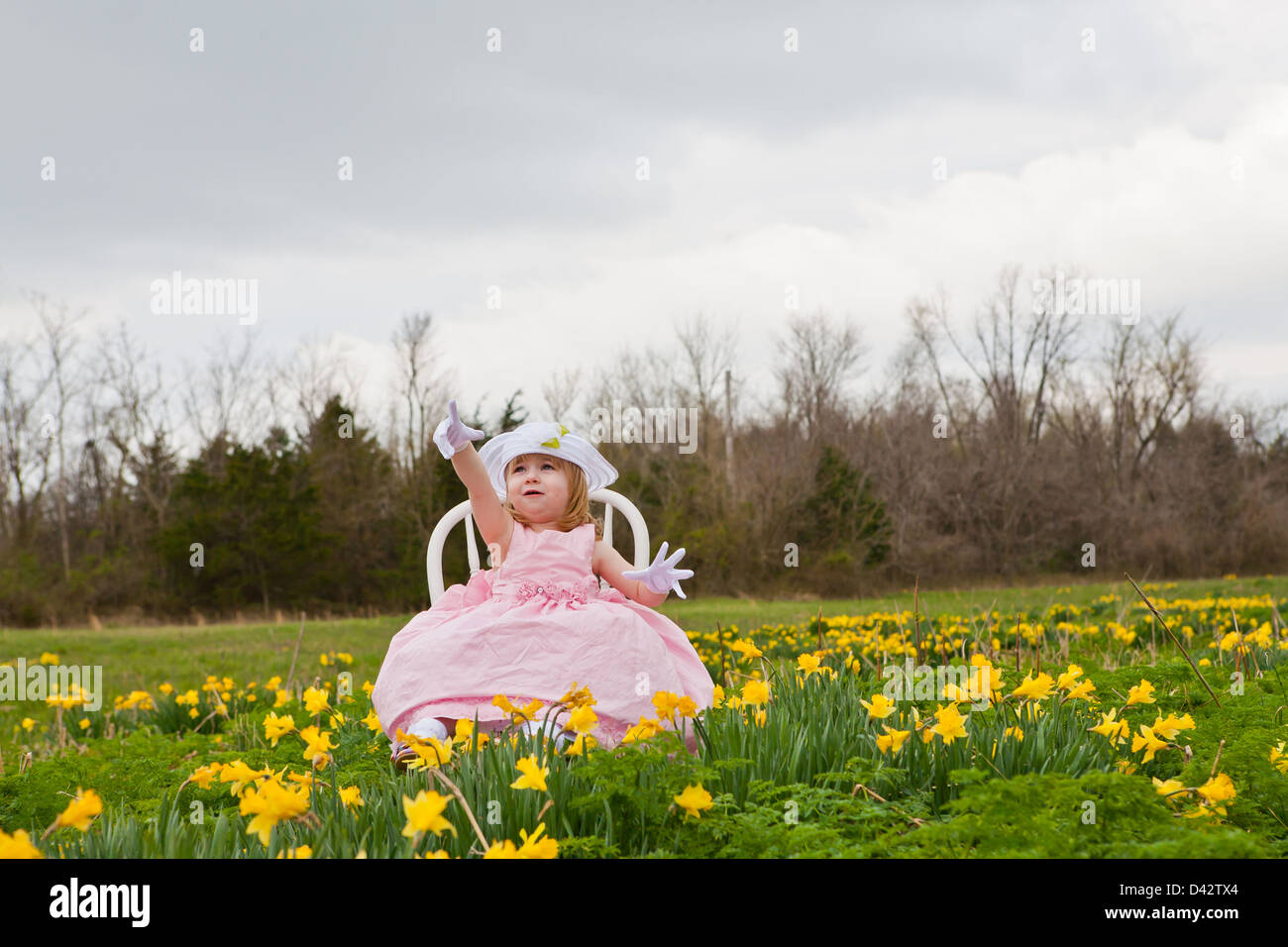 A little girl in a pink dress, white gloves, and white hat, sitting on ...