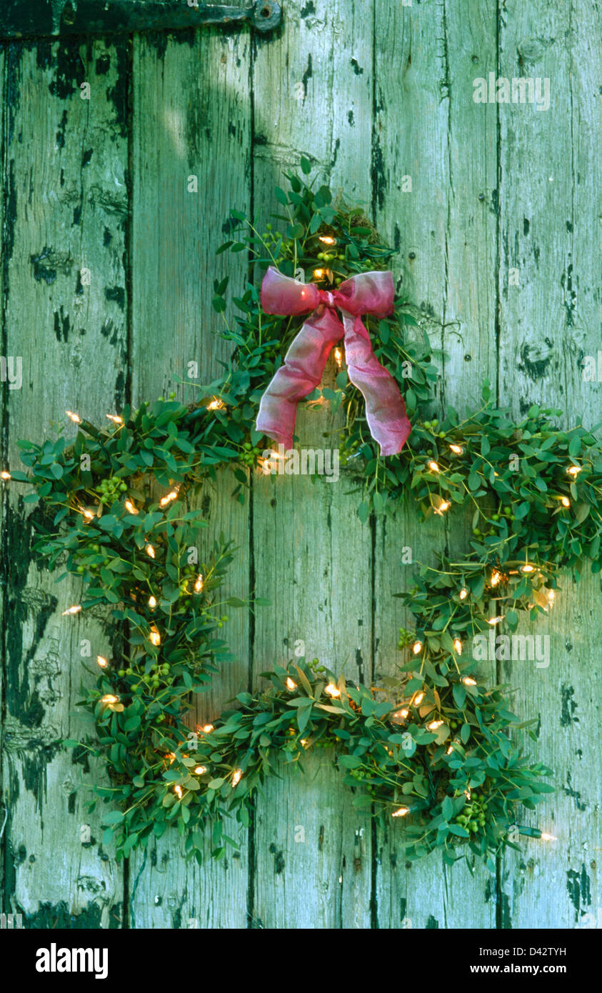 Close-up of home-made star-shaped eucalyptus leaf Christmas wreath decorated with miniature lights and tied with a pink bow Stock Photo