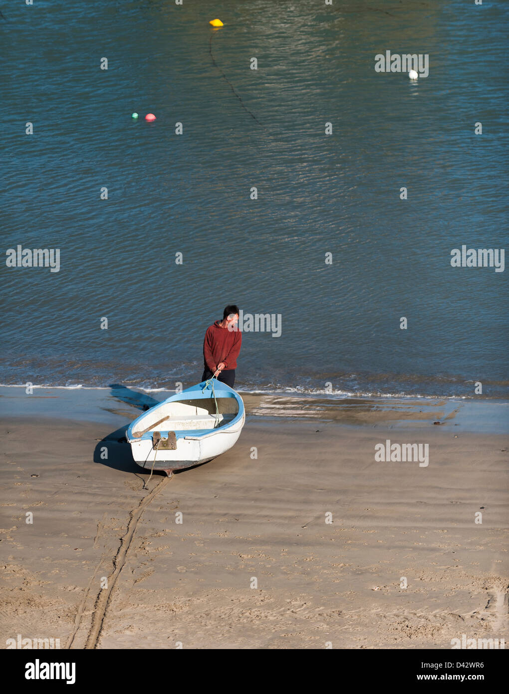 A man dragging a dinghy into the sea. Stock Photo