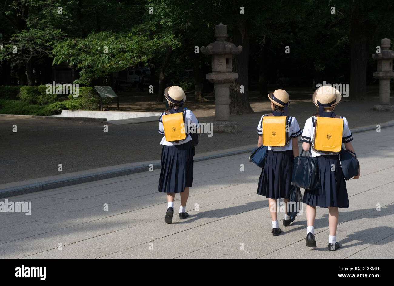 Three Japanese middle school girls wearing sailor uniforms and cute hats walking on their way home from school in Tokyo. Stock Photo