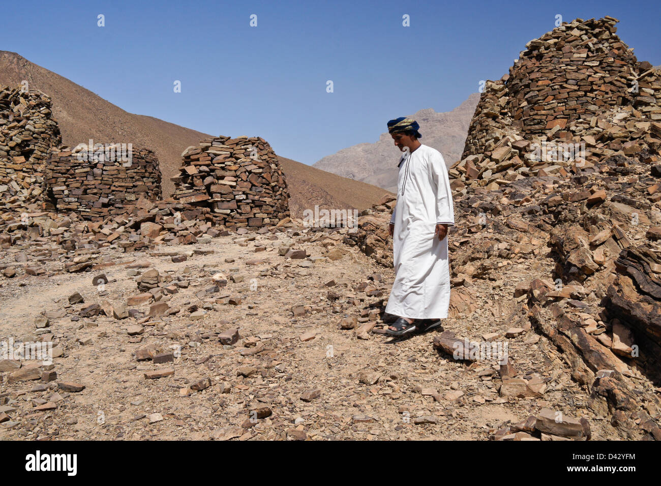 Omani man and Qubur Juhhal beehive tombs at Al-Ayn, Oman Stock Photo