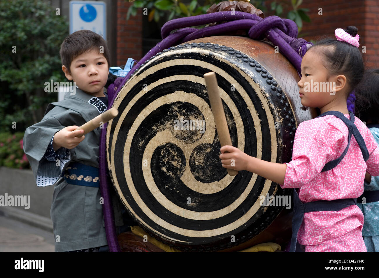 A boy and girl in festival attire join in the fun by beating a taiko drum during the Sanja Matsuri Festival in Tokyo. Stock Photo