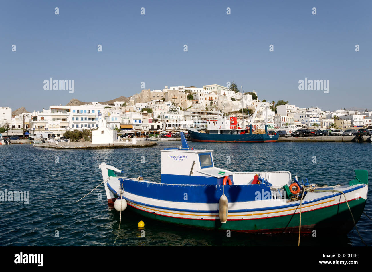 Naxos. Cyclades. Greece. A small docked fishing boat in the harbour of Chora (Naxos town) which rises in the background. Stock Photo