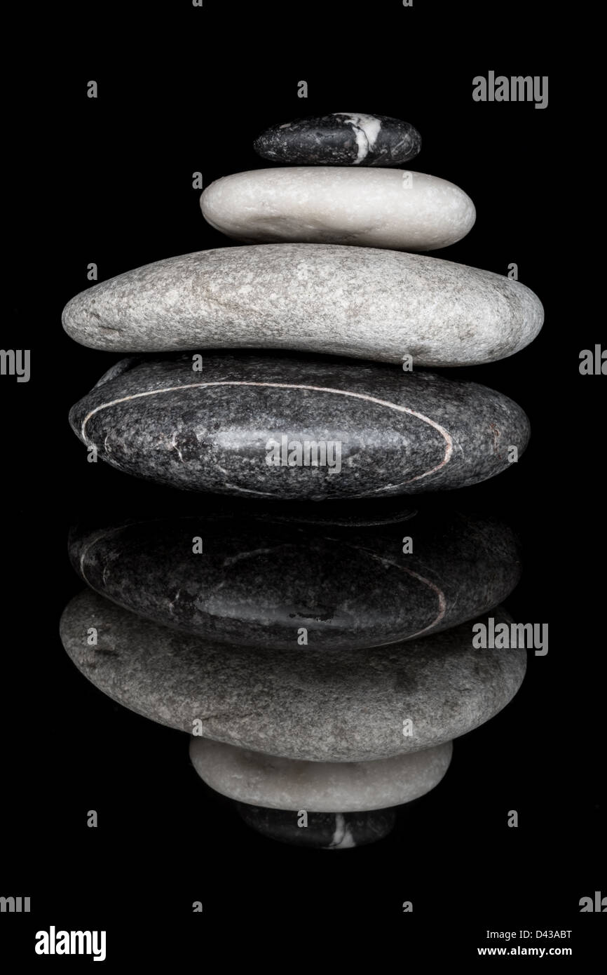 Black & White Close Up Image of a Stack of Four Pebbles on a Black Background, Relected on a Black Surface. Stock Photo