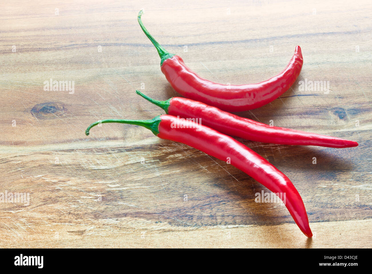 Three red chili peppers on a wooden board Stock Photo