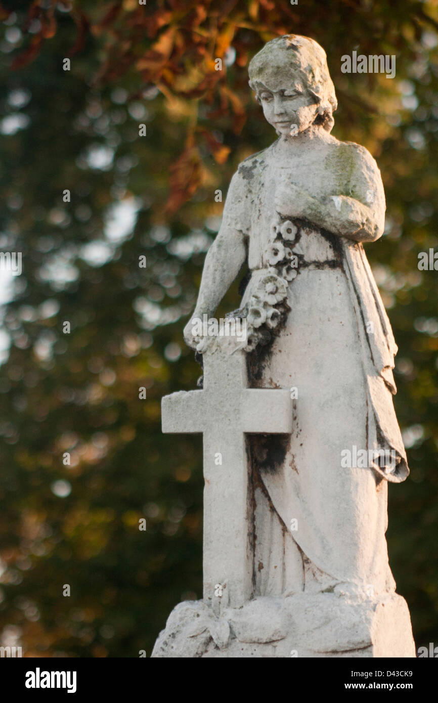 Old statue of a little girl with the cross in the cemetery Stock Photo
