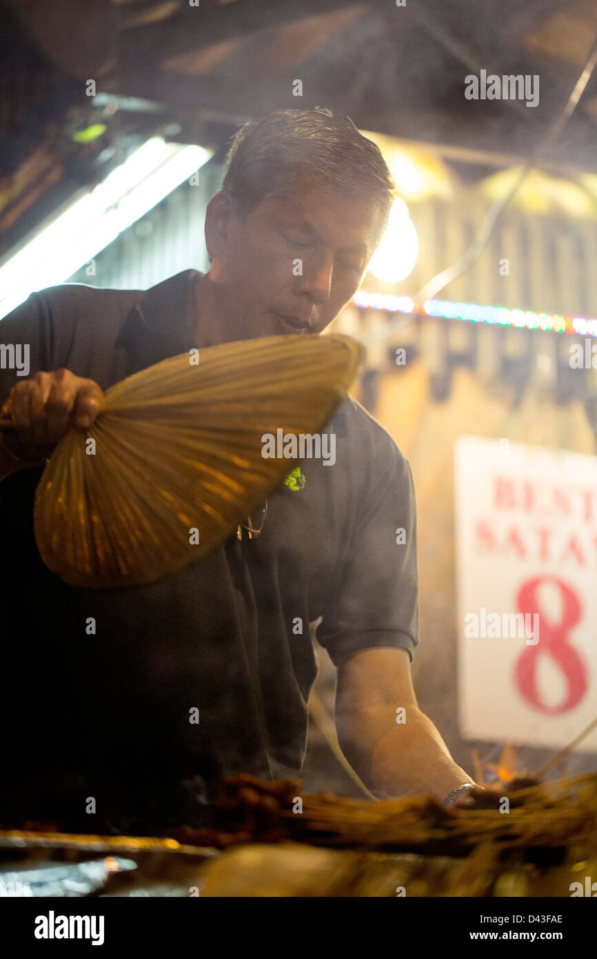 SINGAPORE - 2013:  Satay Street at Lau Pa Sat hawker food market. Satay chef fans his barbecue grill. Stock Photo