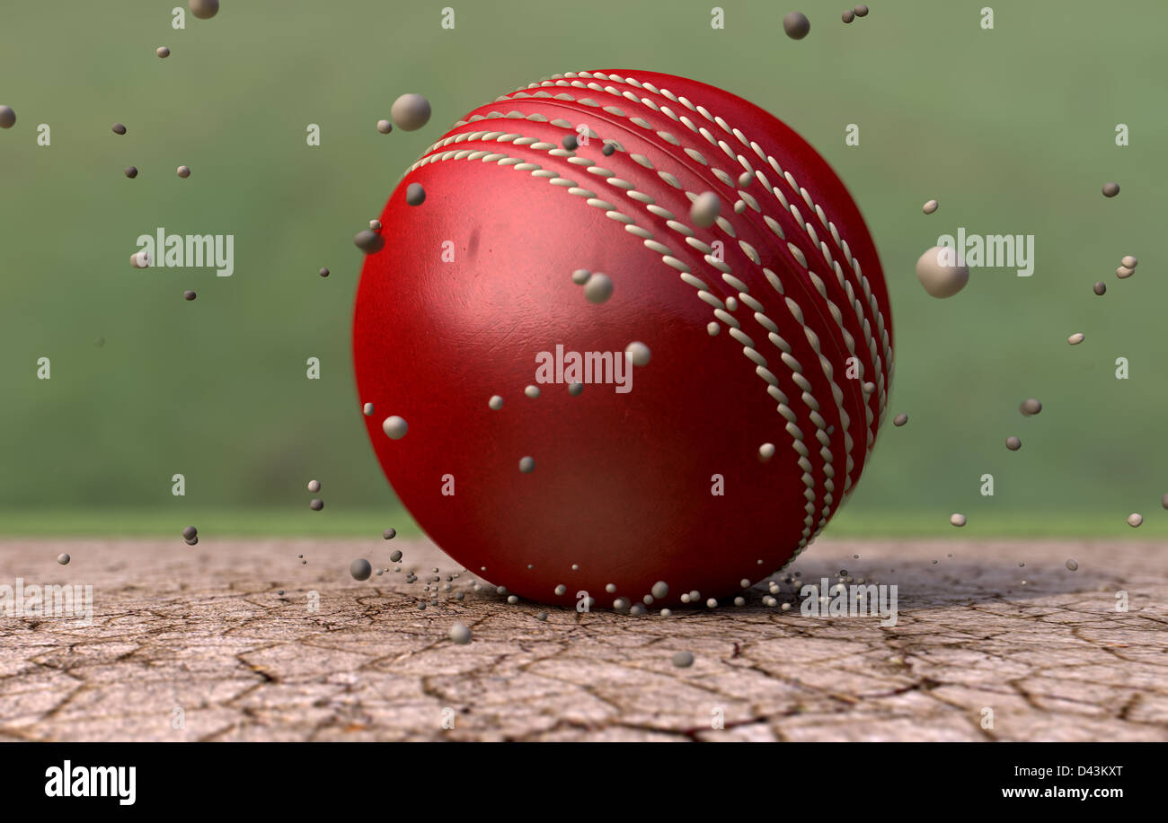 A red leather stitched cricket ball hitting a cracked cricket pitch with dirt particles emanating from the impact Stock Photo
