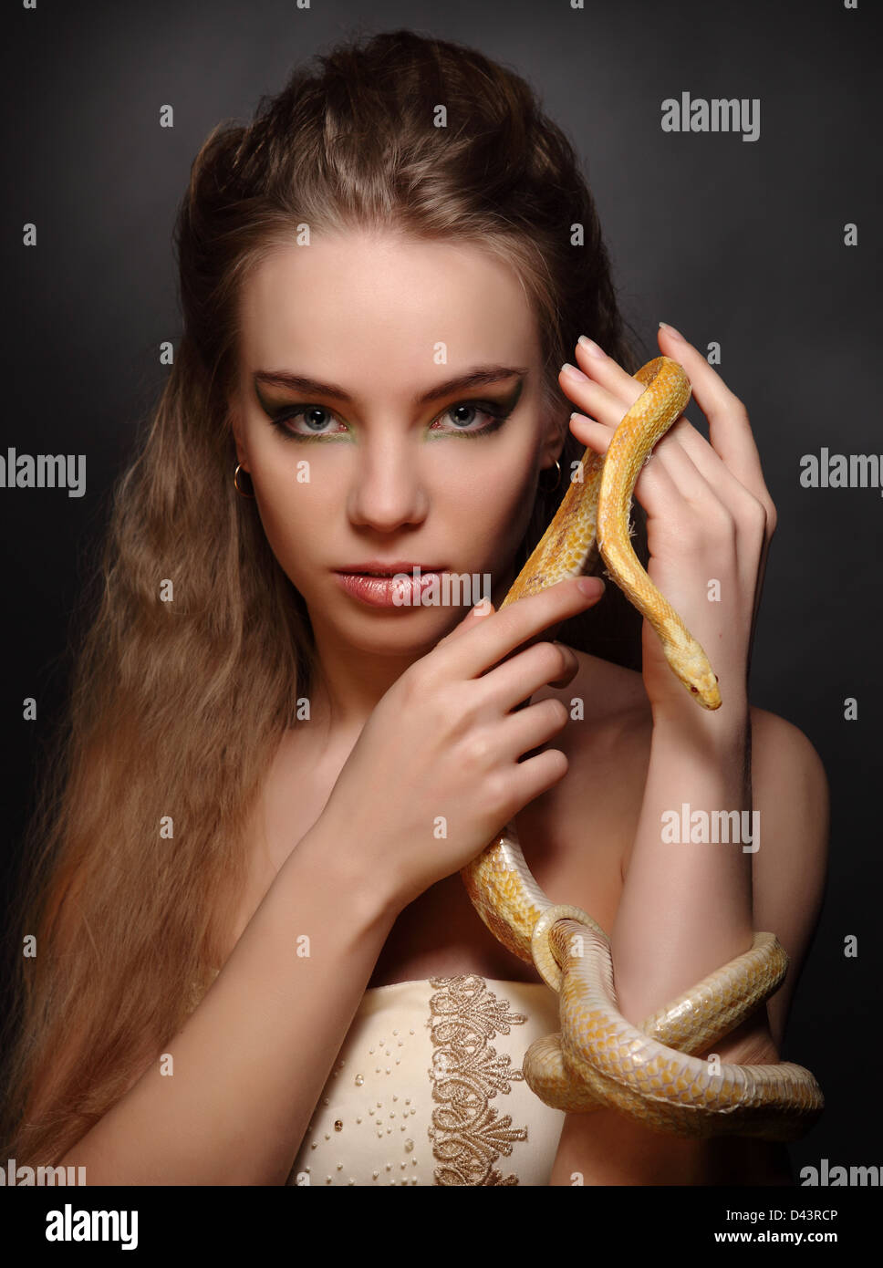 portrait of young woman with yellow snake on dark background Stock Photo