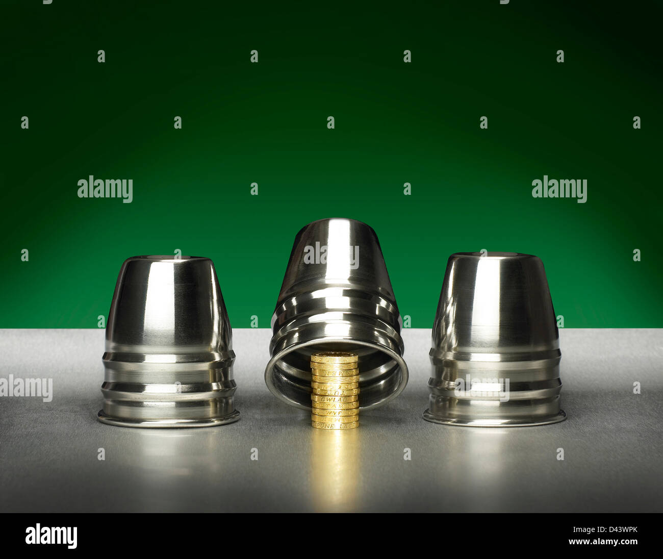 Three silver cups covering golden coins cut out green and silver background Stock Photo