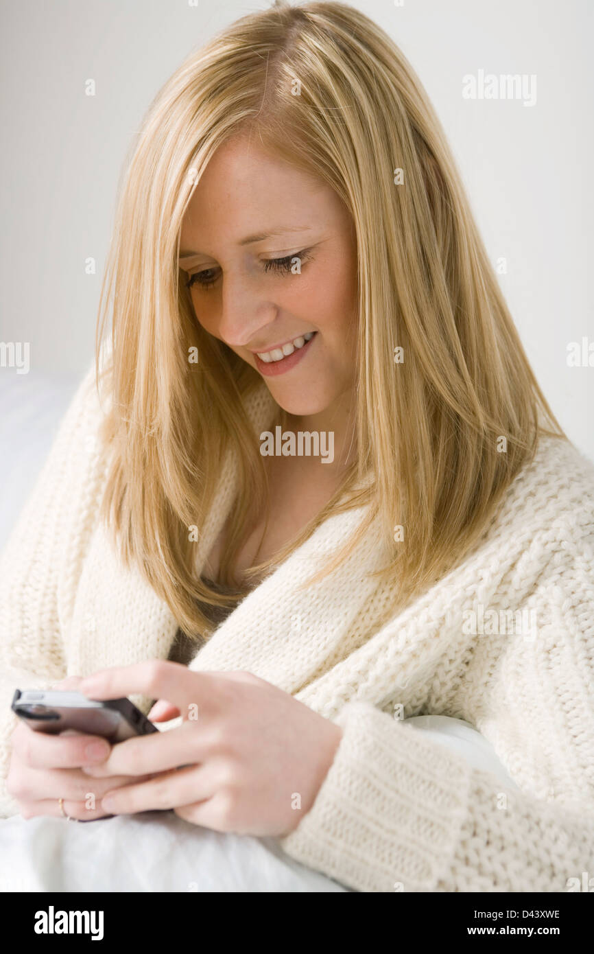 Pretty blonde woman holding a mobile phone sitting on a sofa. Stock Photo