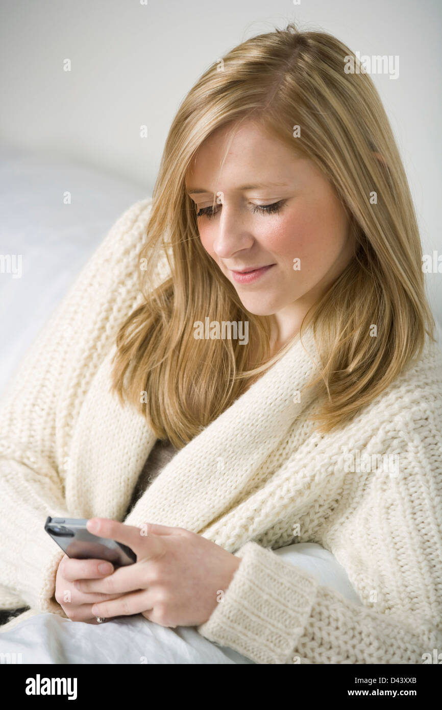 Pretty blonde woman holding a mobile phone sitting on a sofa. Stock Photo