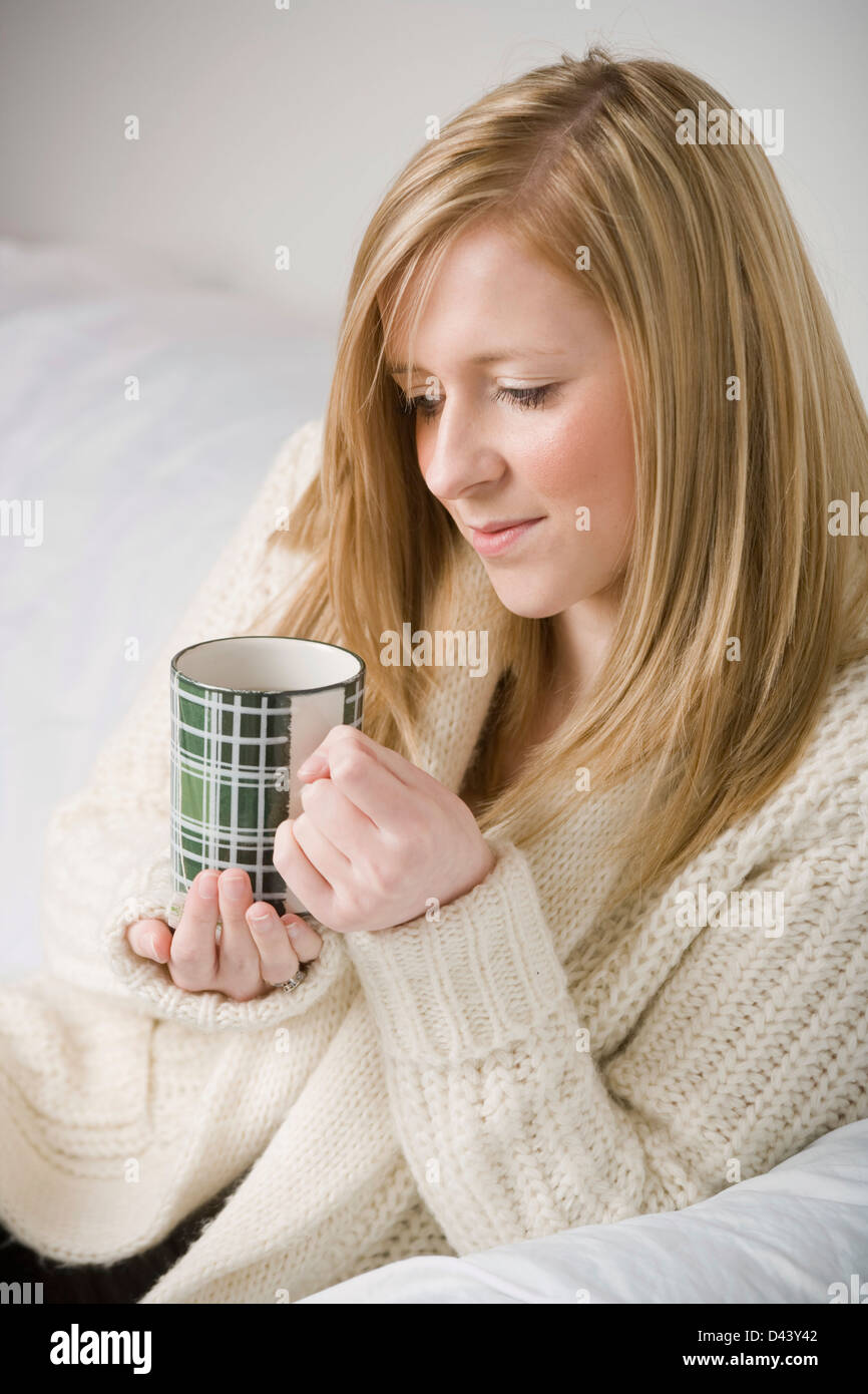Young blonde woman relaxing with a cup of tea on a sofa. Stock Photo