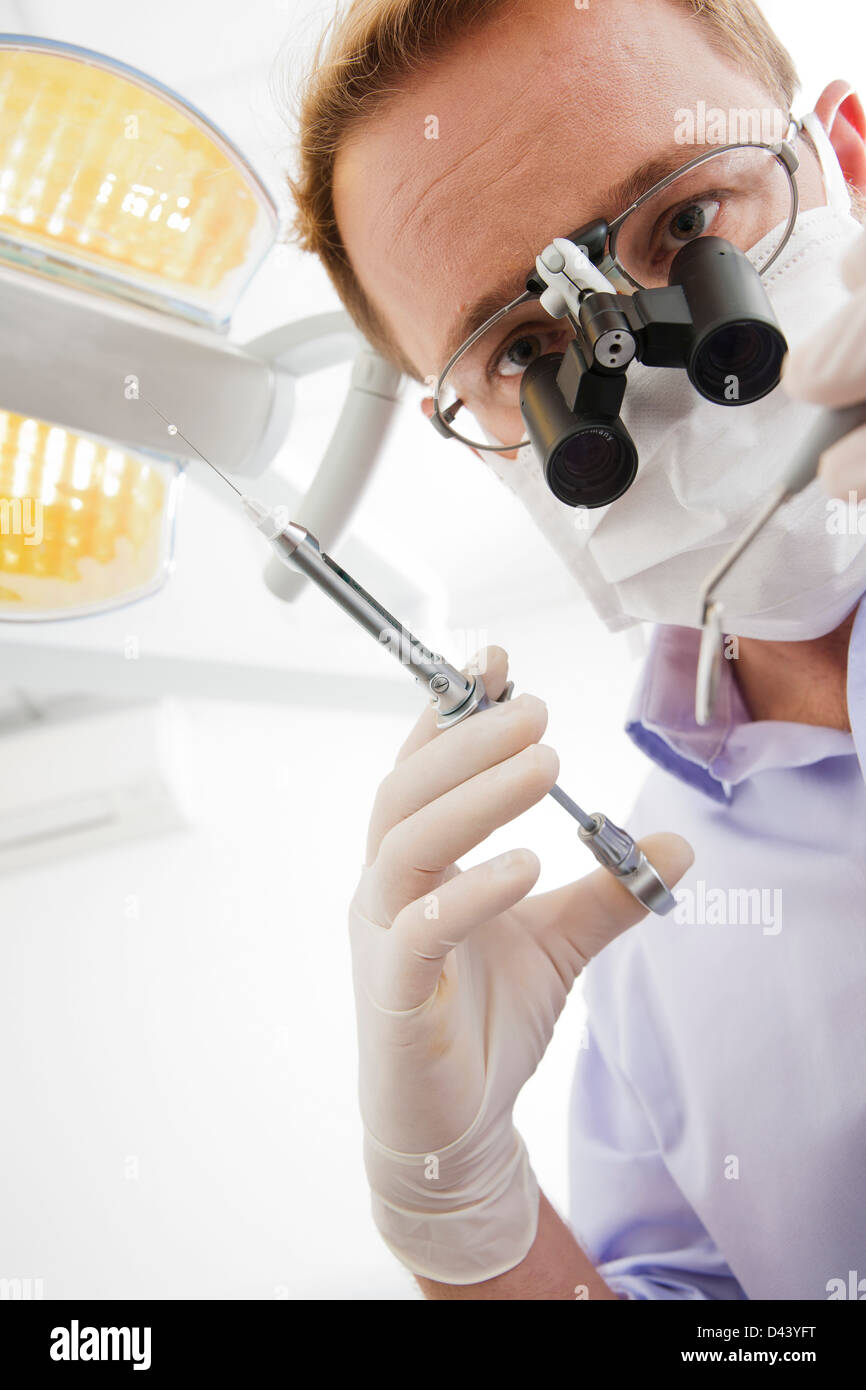 Dentist wearing Surgical Mask and Magnifier holding Needle and looking