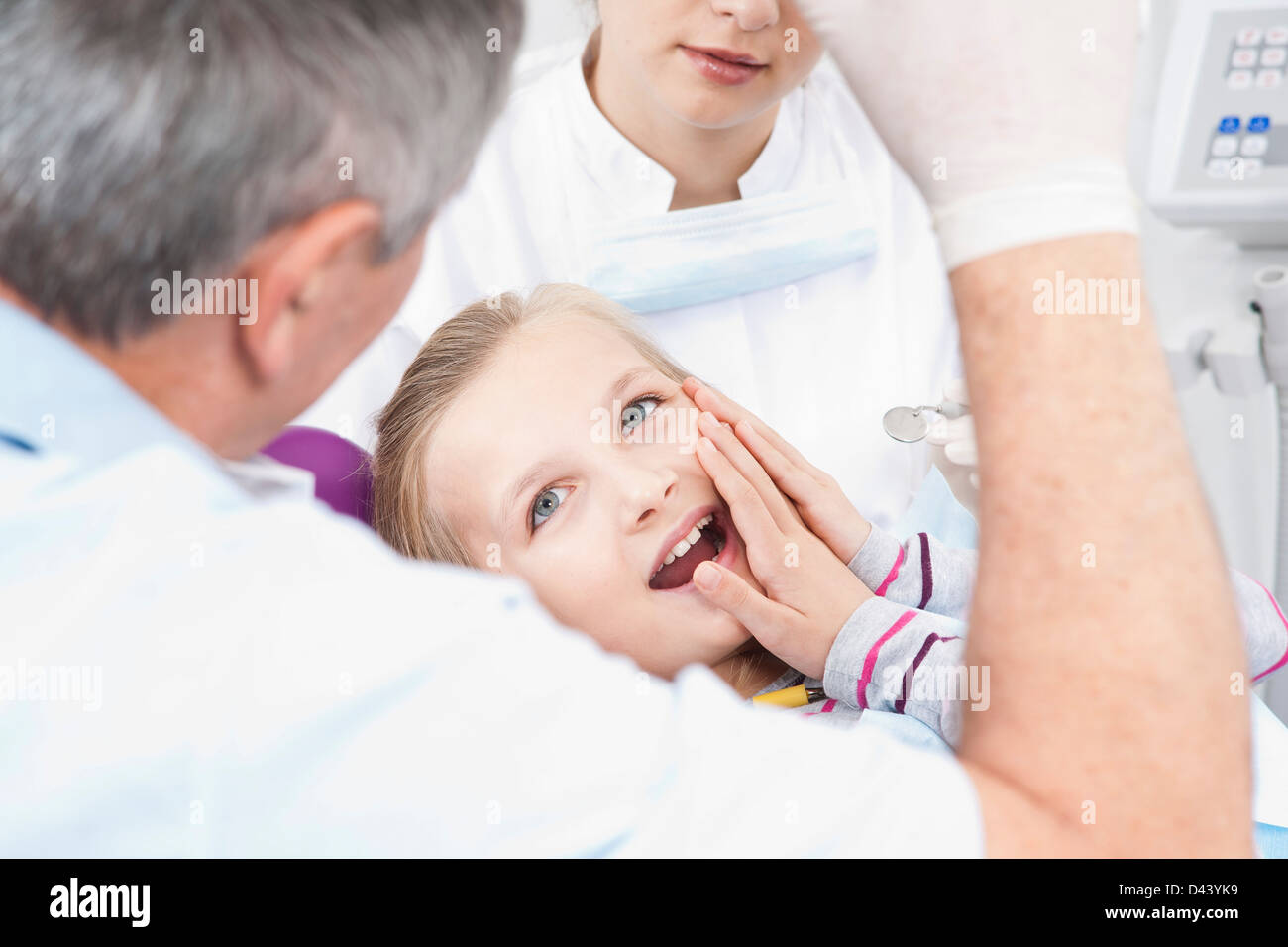 Girl touching Cheek with Dentist and Hygienist in Dental Office