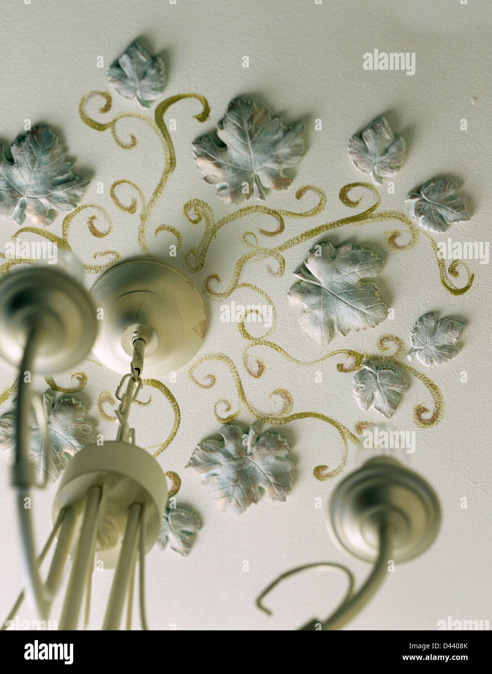 Hand-painted plaster ivy leaves and gold decoration on ceiling around light fitting Stock Photo