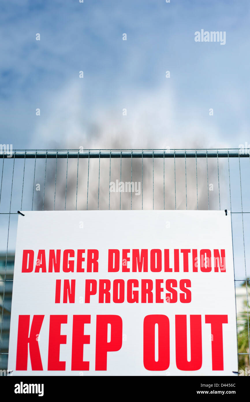 Sign reading ' Danger Demolition in Progress KEEP OUT ' with rising smoke behind it, UK Stock Photo