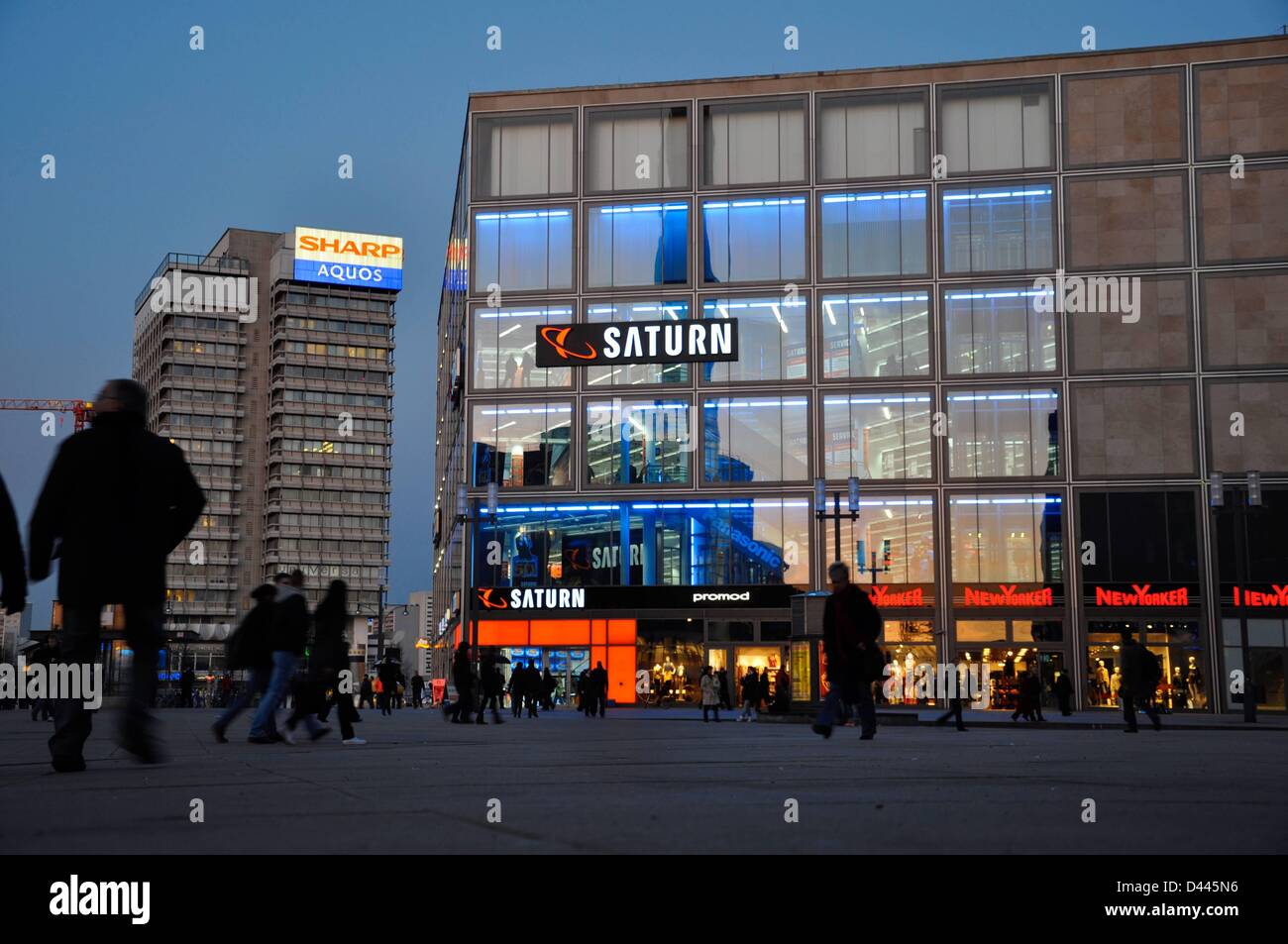 People walk in front of a branch of the consumer electronics retailer Saturn at Alexanderplatz in Berlin, Germany, 7 March 2011. In the background, the Haus des Reisens (House of Traveling) is pictured with the neon writing 'Sharp Aquos'. During the GDR era, the building housed the GDR travel agent 'Interflug'. Fotoarchiv für ZeitgeschichteS.Steinach Stock Photo