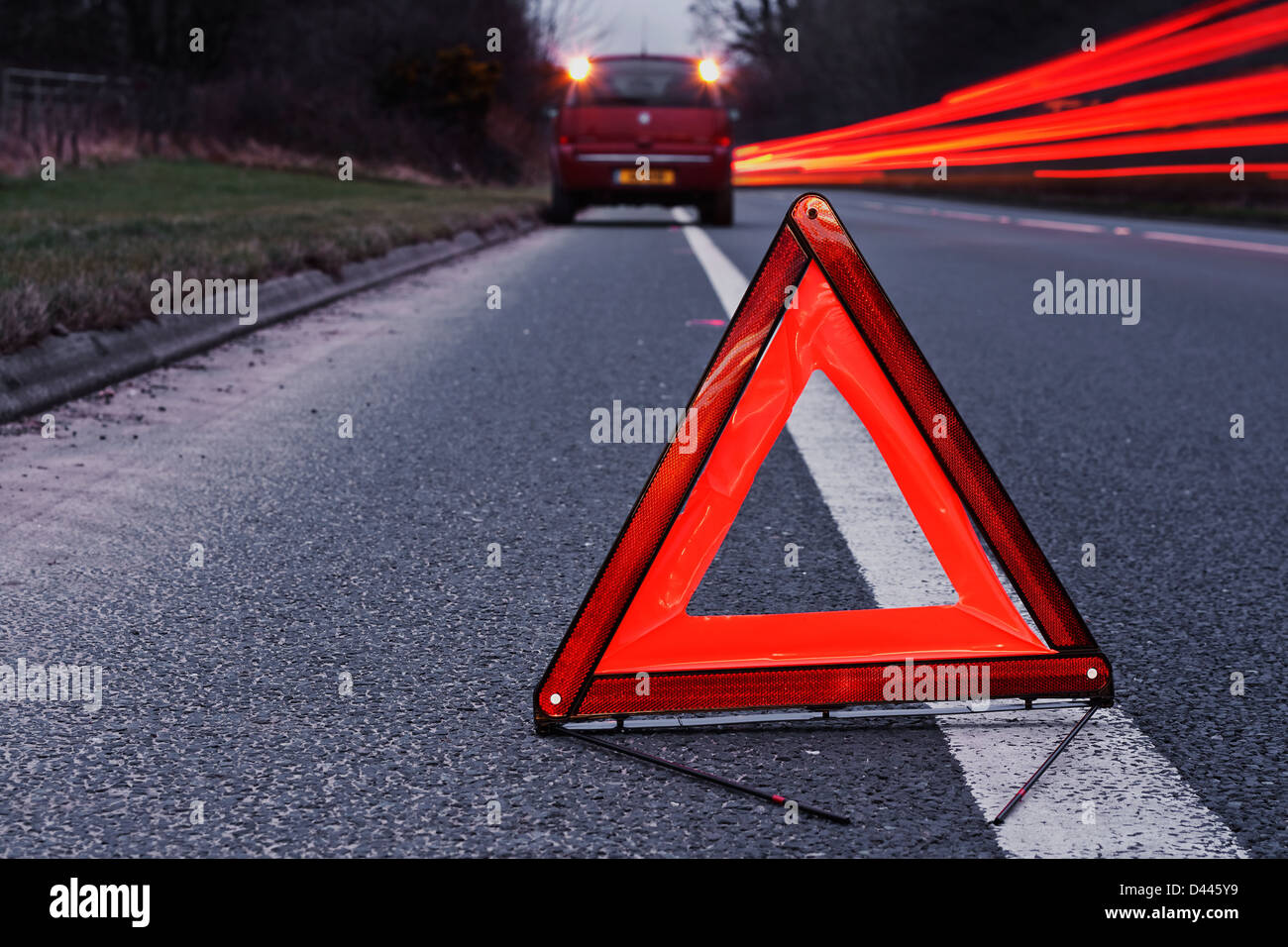 broken down car dangerously parked awaiting recovery services at the side of a busy highway at night with cars rushing past Stock Photo