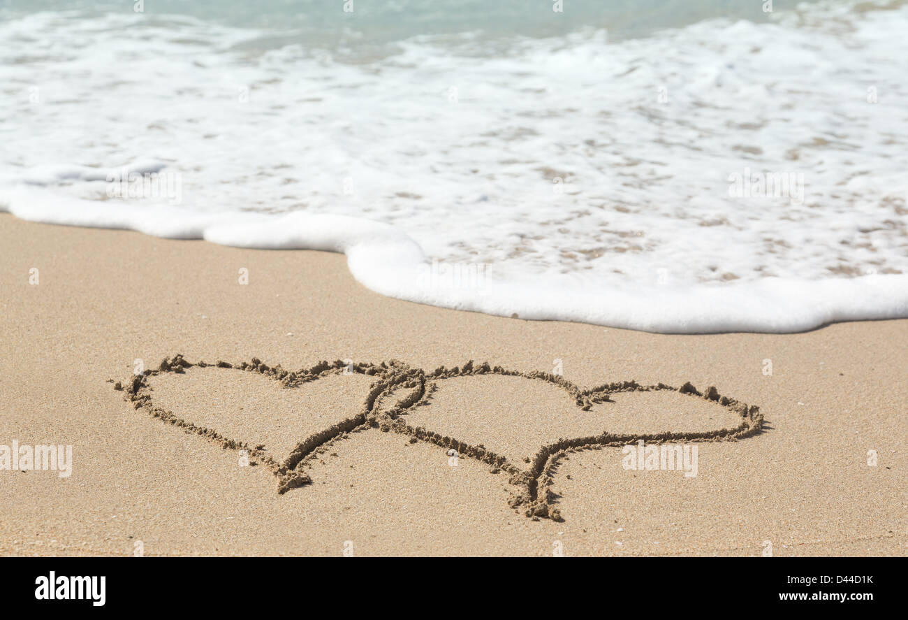 Linked love hearts drawn in the sand on a tropical beach by ocean surf - love holiday vacation romance concept Stock Photo