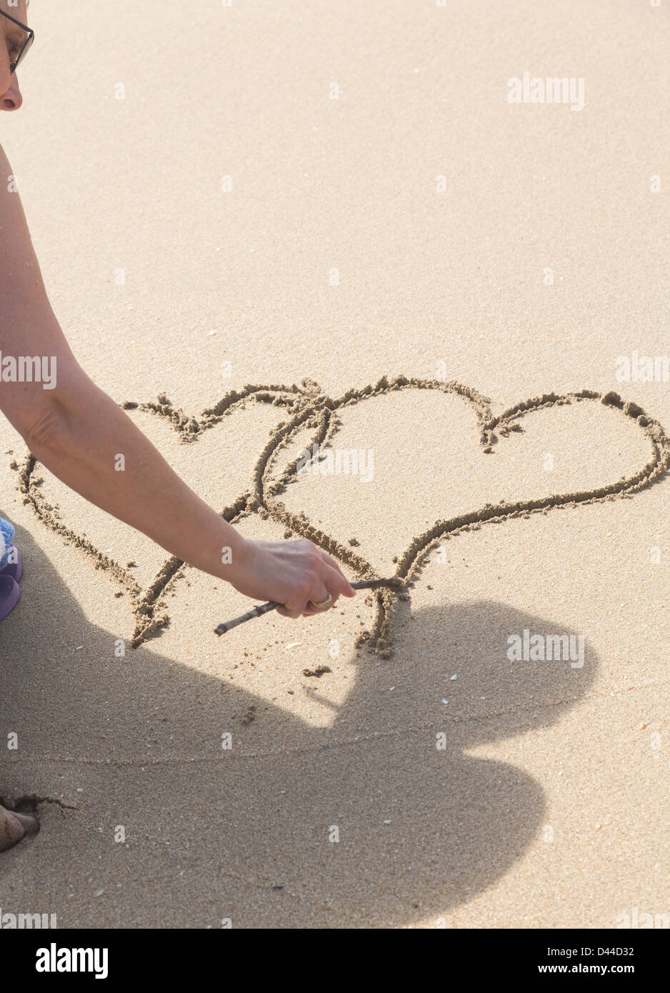 Lady drawing pair of linked hearts in sand on beach in Caribbean Stock Photo