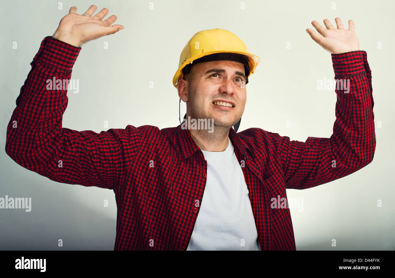 Construction worker in red shirt and yellow hardhat with raised hands Stock Photo
