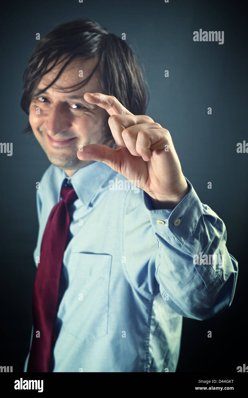 Smiling businessman is mocking, showing a small sign with his fingers. Mock, gibe, jeer, ridicule concept. Stock Photo