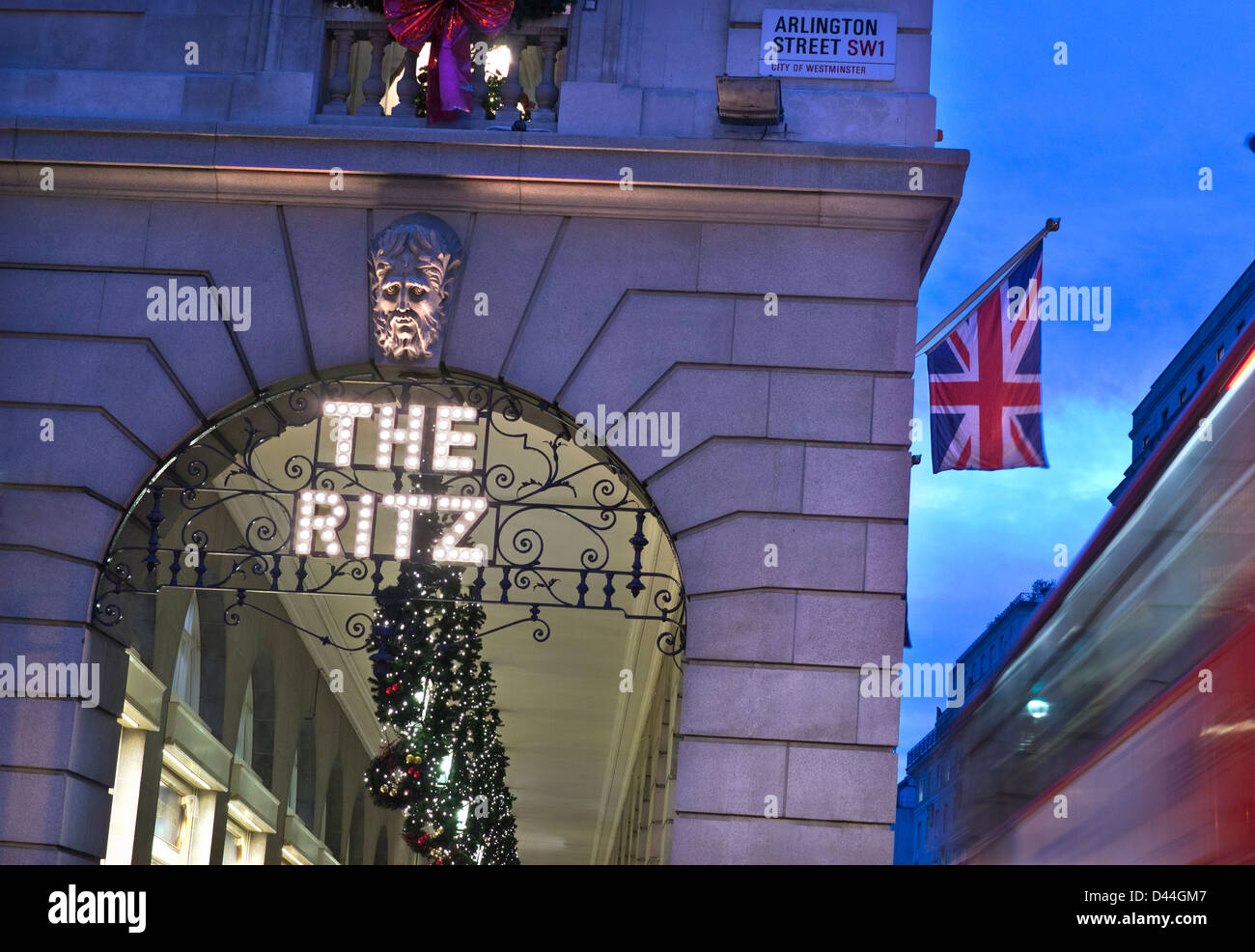 The Ritz Hotel London at dusk exterior lights name with Christmas decorations Union Jack flag and blurred passing red bus Piccadilly London UK Stock Photo