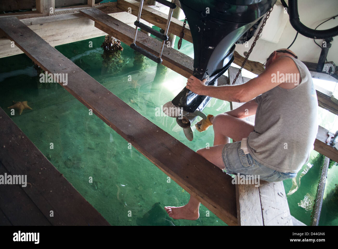 Mechanic working on a boat engine that is hanging over saltwater with