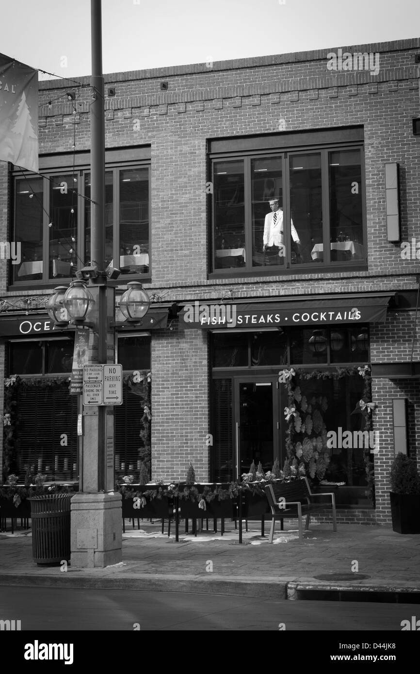A waiter peers out of the second floor window of a restaurant looking for patrons to serve at Ocean Prime Restaurant Stock Photo