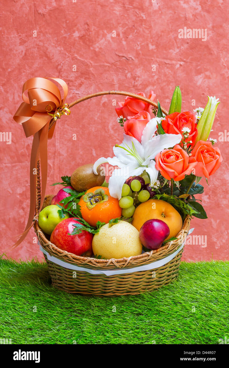 Basket of fruit and flower on green grass and grunge wall Stock Photo