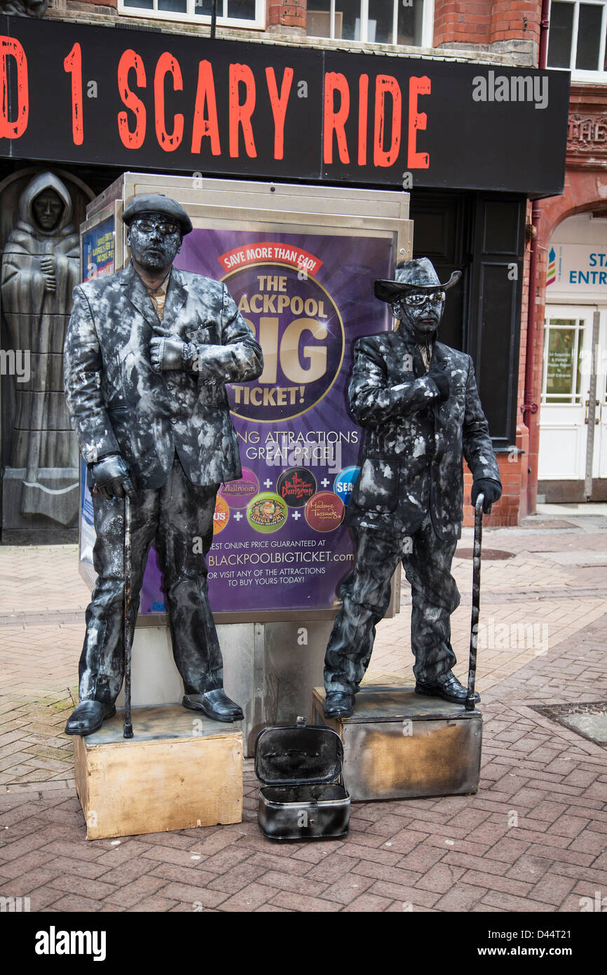 Scary Ride, Two dark suited men; Man standing still crowd costumed figures acting as Statues splashed with white paint, outside Blackpool attraction, Stock Photo