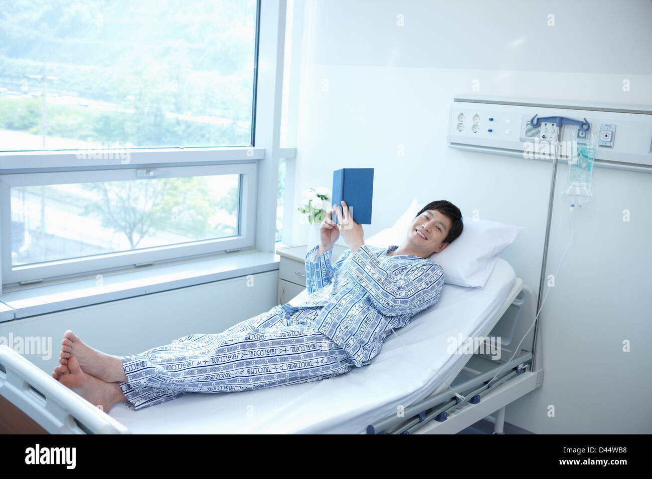 a patient lying on the bed reading a book in hospital room Stock Photo