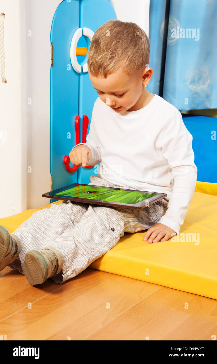 Blond five years old boy occupied with tablet computer touching screen