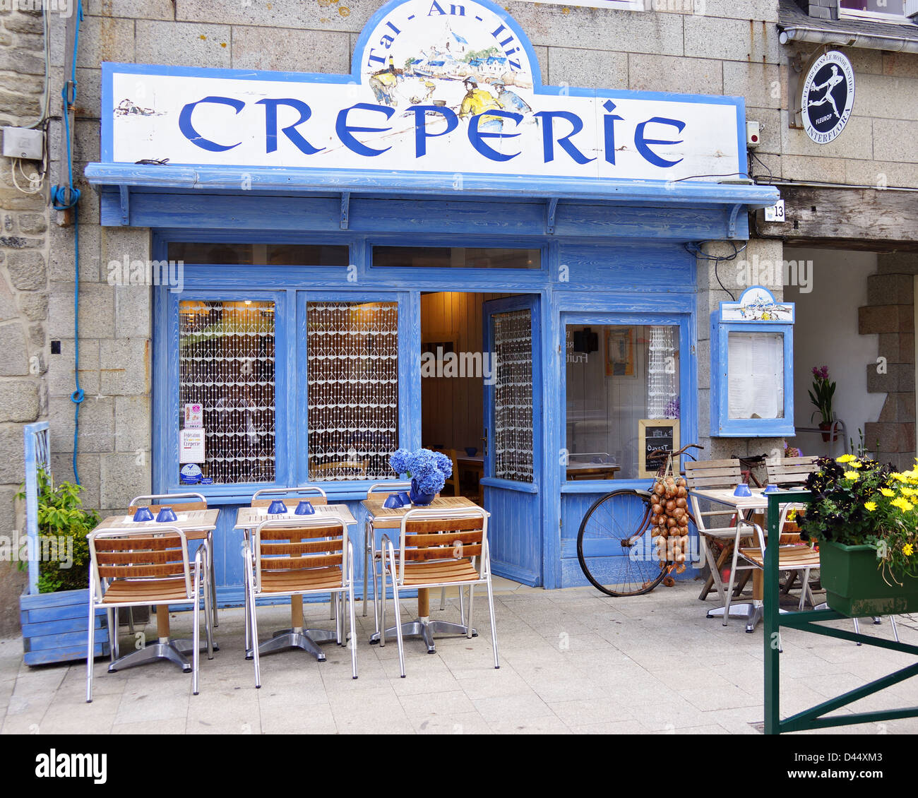 French Creperie shop front with tables outside including an old bike with string of onions hanging from it Stock Photo