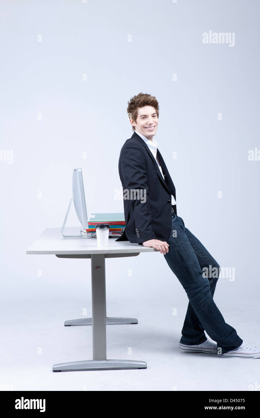a man sitting on a desk smiling Stock Photo - Alamy