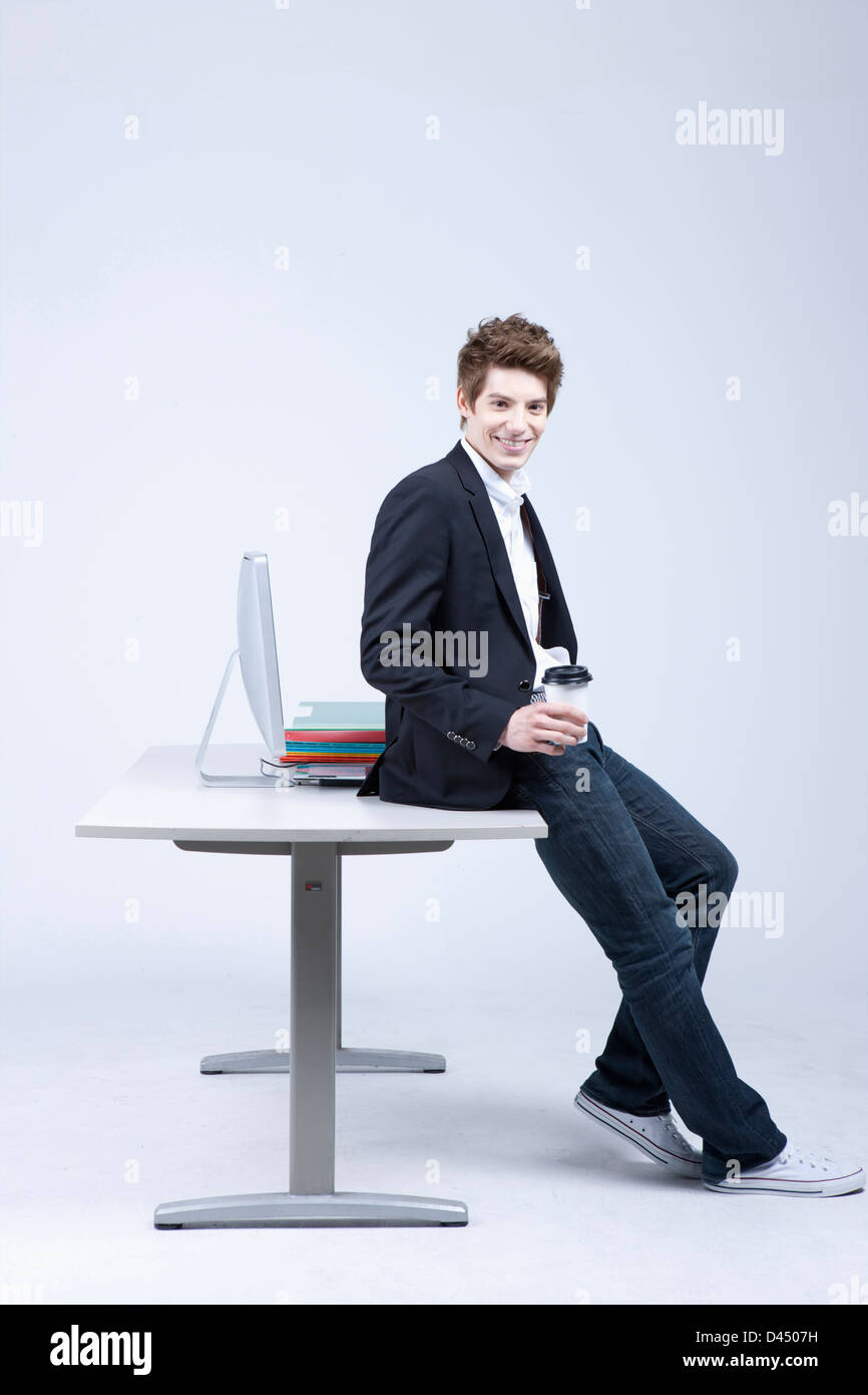 a man sitting on a desk smiling Stock Photo - Alamy