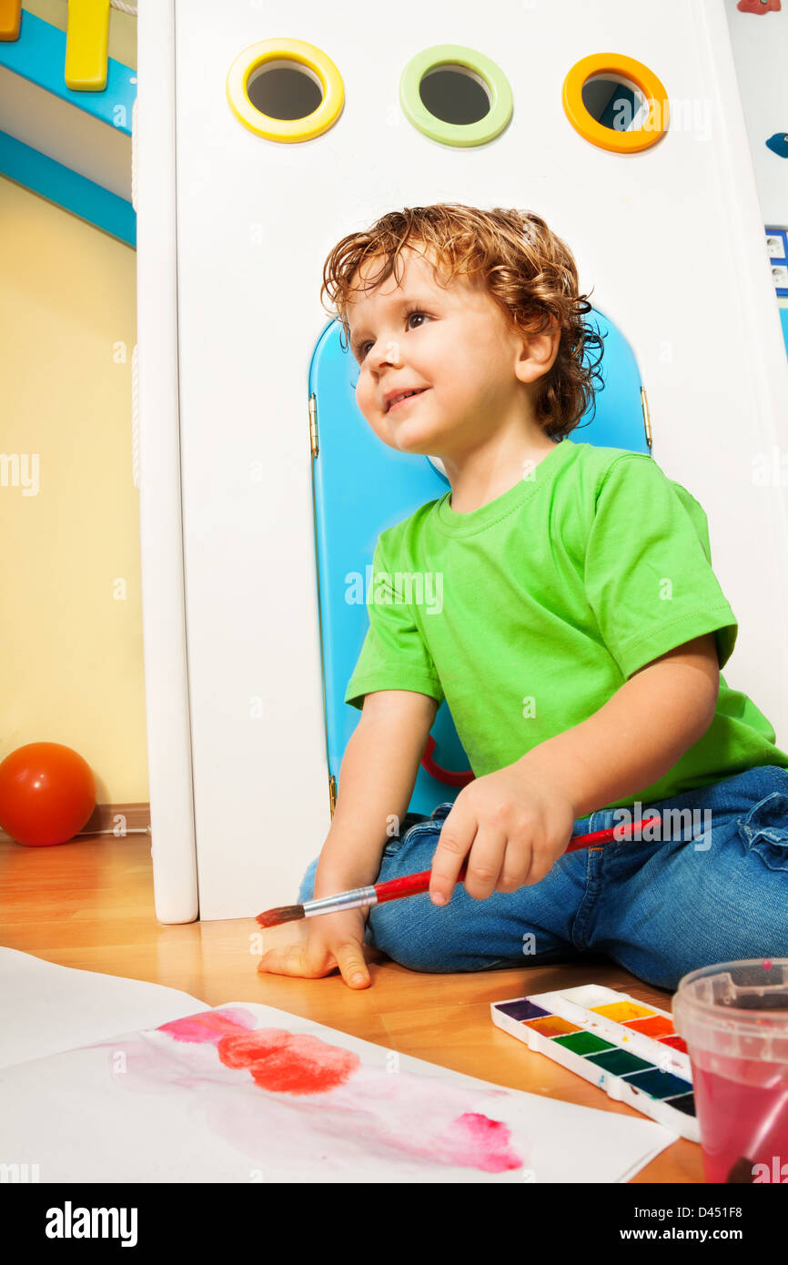 Two years old boy painting with watercolors sitting on the floor in kids room Stock Photo