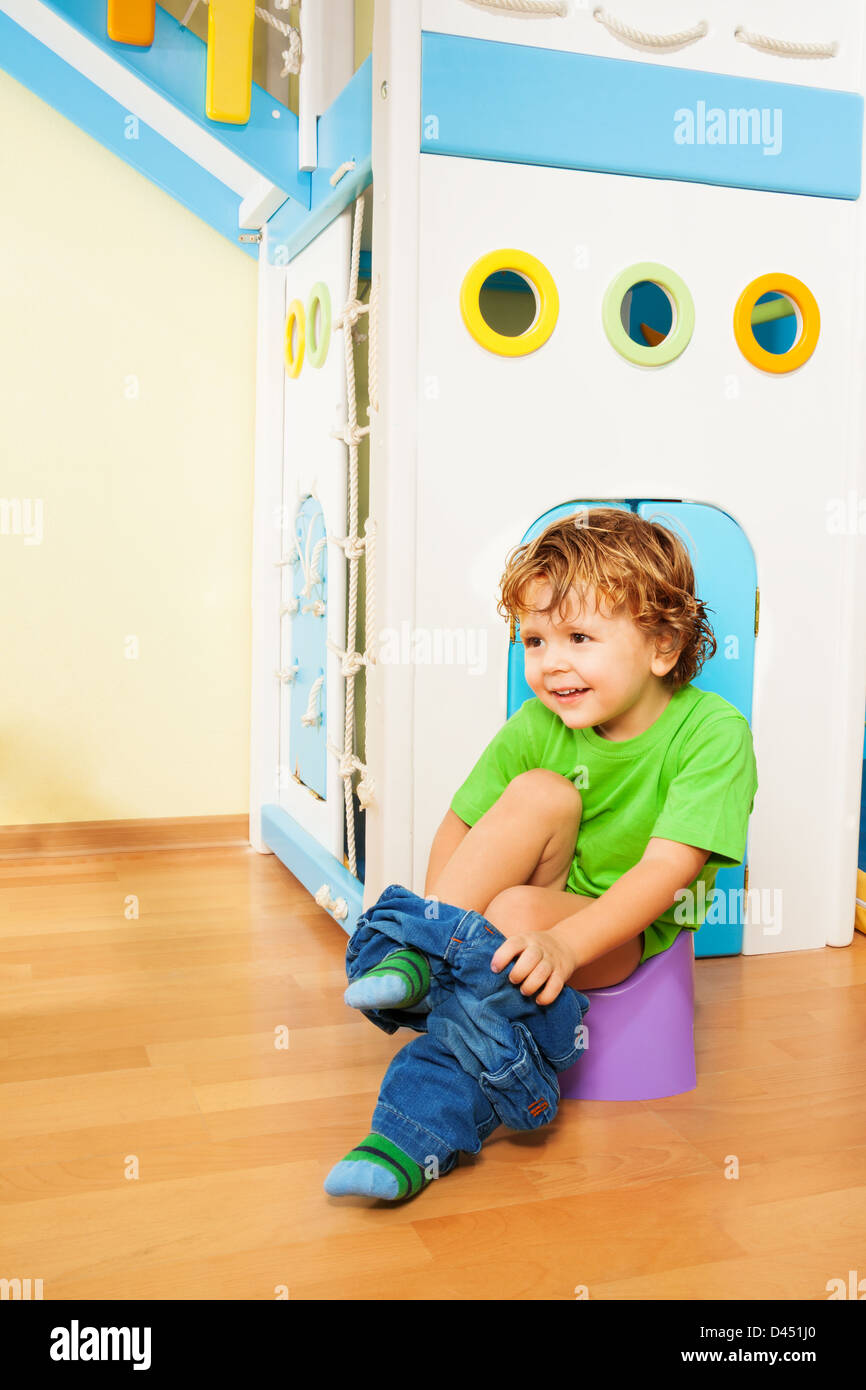Small two years old boy putting off his pants as he learns to use a ...