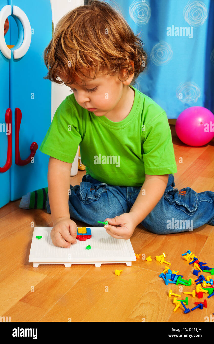 Little two years old boy solving puzzle assembling mosaic sitting on the floor in his room Stock