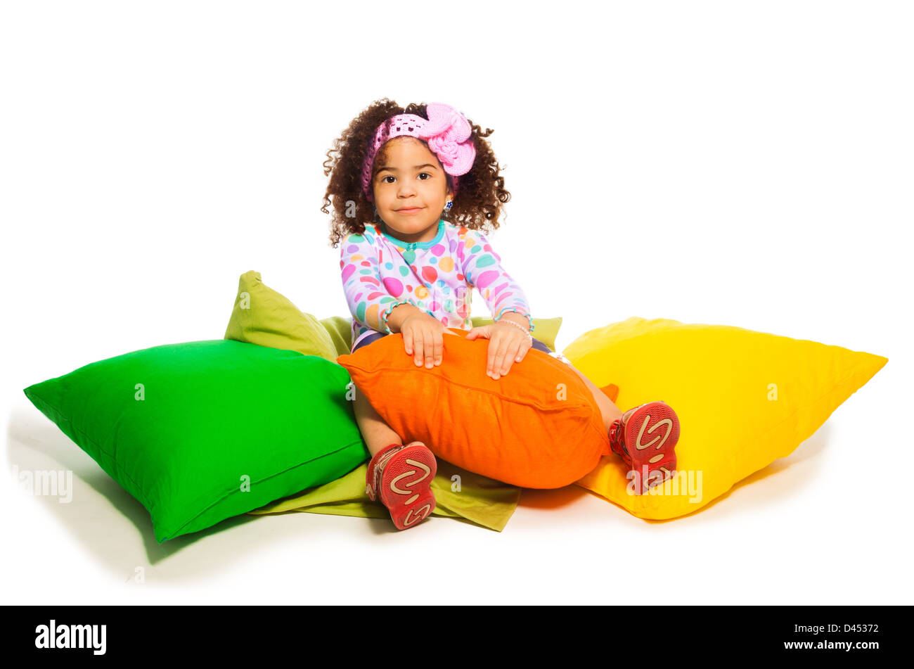 Cute black curly two years old girl sitting in the pillows, isolated on
