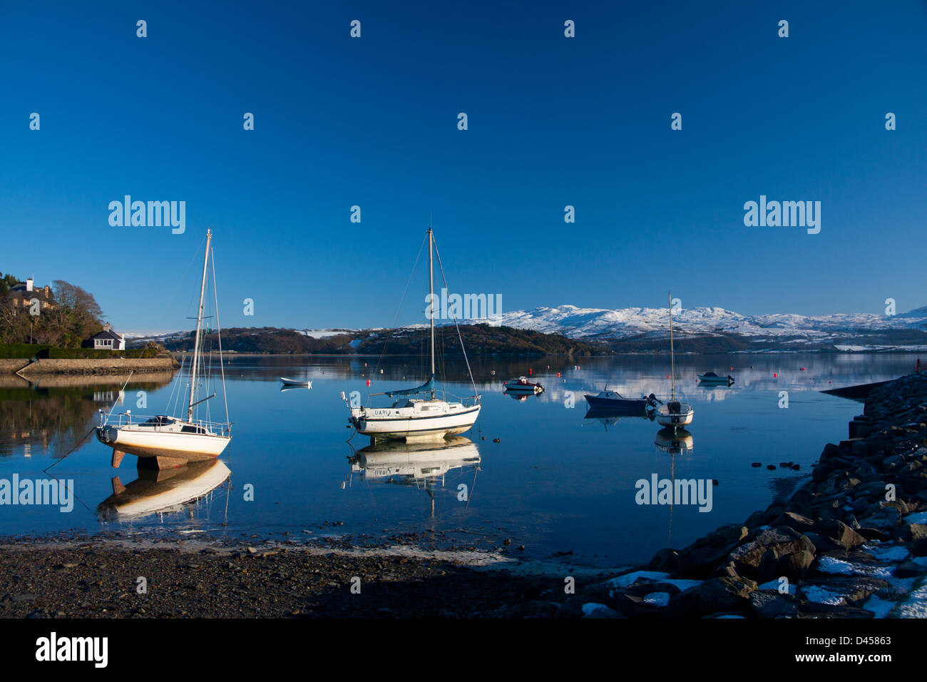 Boats in Borth-y-Gest harbour in winter with snow on mountains in distance Stock Photo
