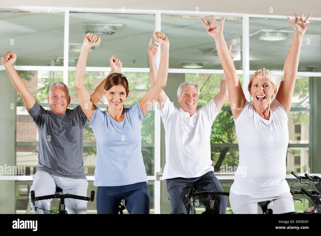 Happy cheering senior group in fitness center on spinning bikes Stock Photo