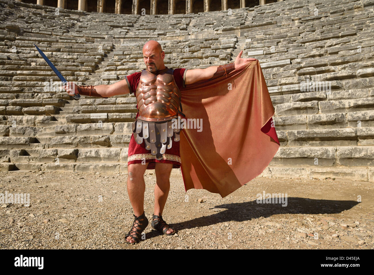 Glowering Roman Gladiator with sword spreading cape in sun on stage at the ancient Aspendos theater Turkey Stock Photo