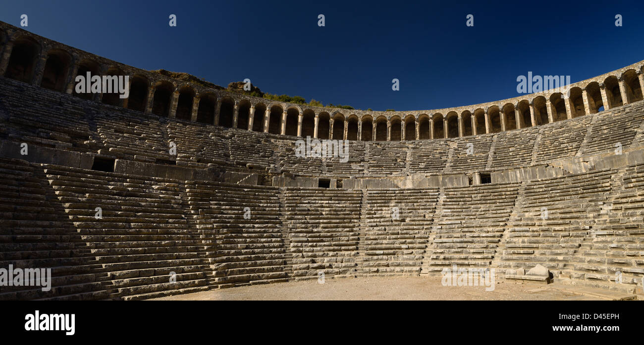 Panorama of semicircular stone seats at ancient Roman theater Aspendos Amphitheatre with upper gallery arches and stage Turkey with blue sky Stock Photo