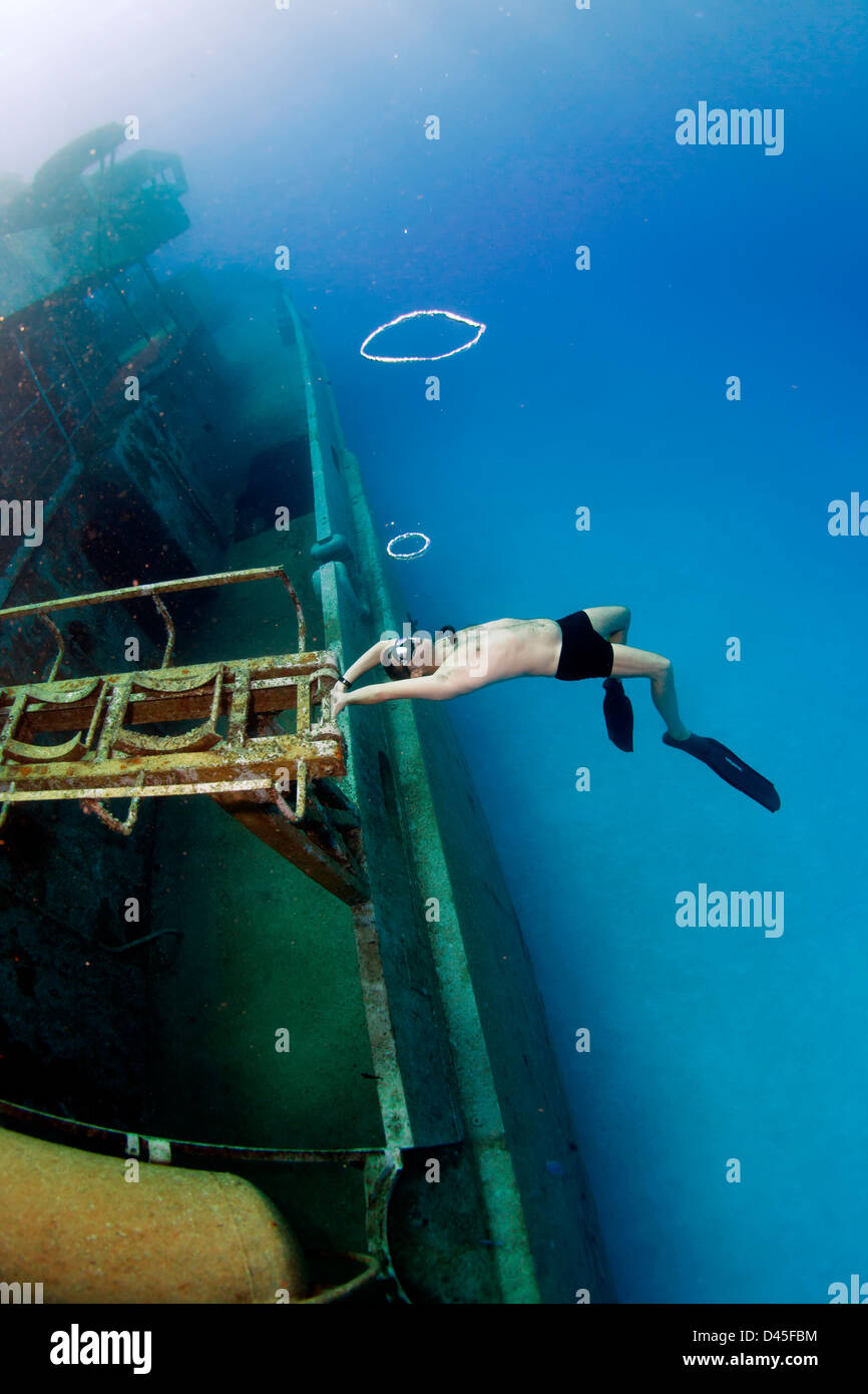 A freediving man blows ring bubbles on the  Kittiwake Shipwreck off Grand Cayman Island. Stock Photo