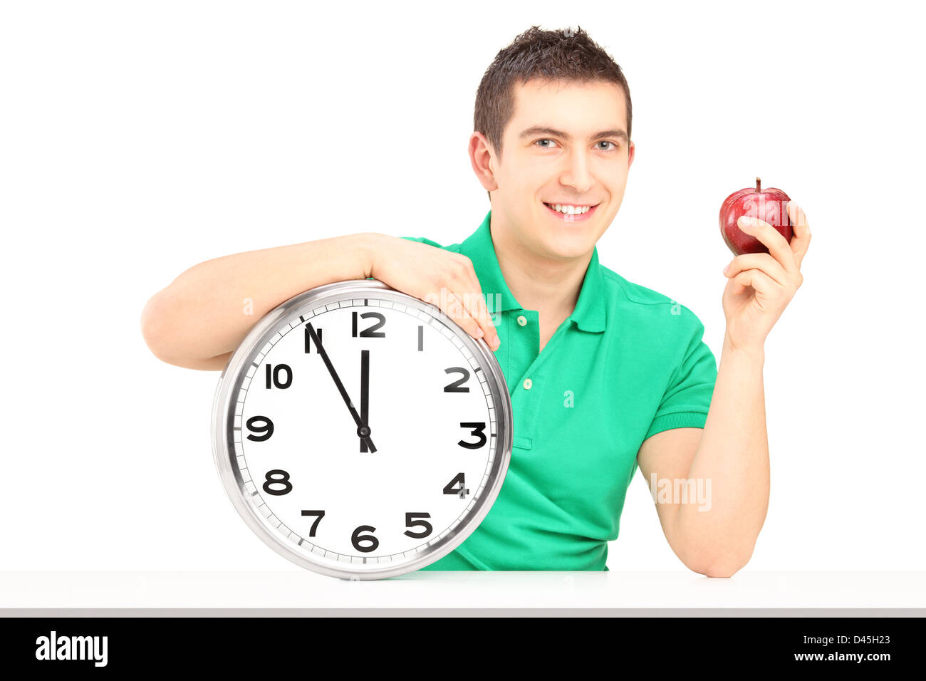 Young man holding wall clock and red apple on a table isolated on white background Stock Photo