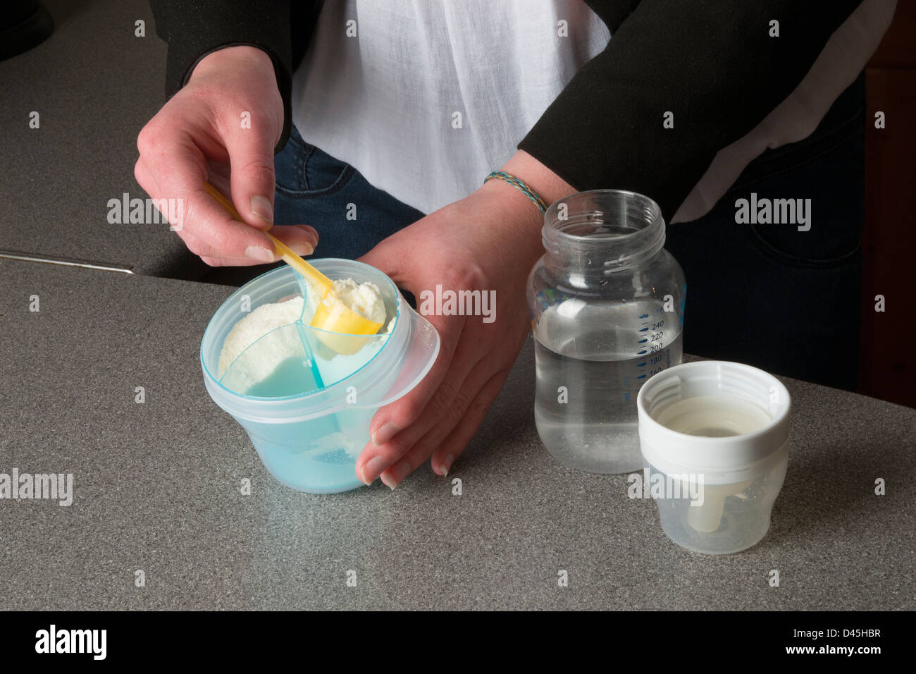 Young mother's hands preparing powdered milk drink for her baby Stock Photo